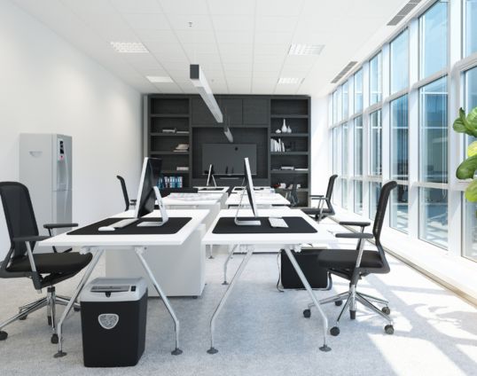 Modernes Büro mit weißen Tischen, schwarzen Stühlen, Computern und großen Fenstern.