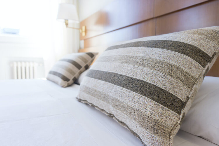 Ein gemachtes Bett mit gestreiften Kissen und einer Wandlampe im Hintergrund.